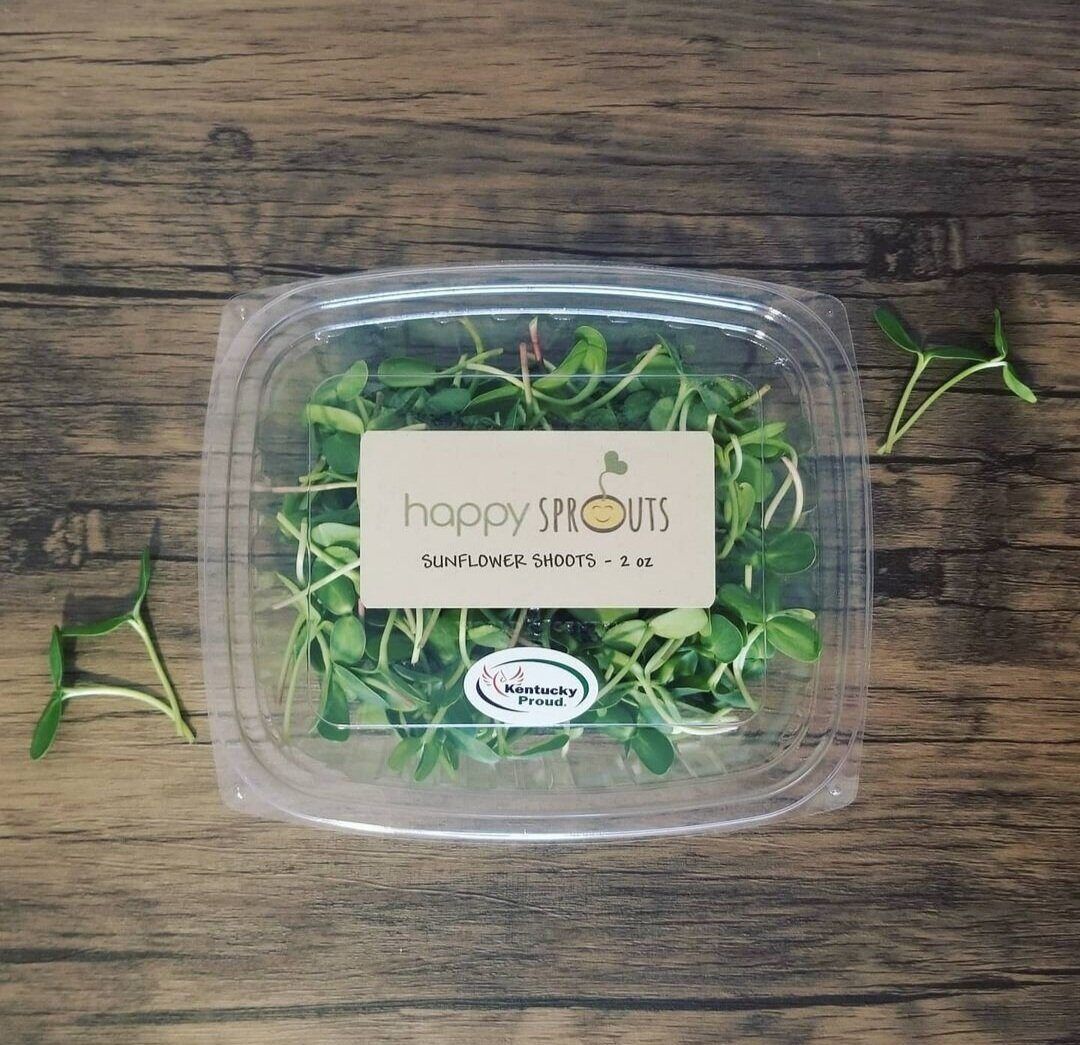 A 2oz clamshell of Happy Sprouts sunflower shoots on a wooden table